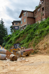 Brick houses on top of hillside with Chinese heavy equipment and barrels by Marie Anna Lee
