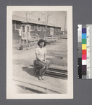 One woman #85 [seated on bench; house in background]