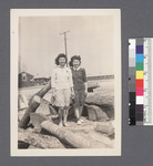 Two women #7 [standing & leaning on woodpile]: Marietta Hatori (L), Helen Oshiro (R) by Richard Shizuo Yoshikawa